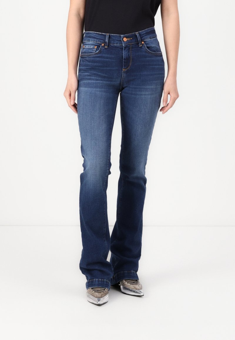 Dark blue flared jeans with subtle fading, five-pocket design, and copper rivet accents, paired with metallic gray shoes.
