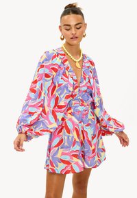 Robe portefeuille colorée à motif floral avec manches longues ballon, encolure en V profonde et accents à volants. Fabriquée en tissu léger.