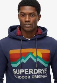 Donkerblauwe hoodie met trekkoorden, voorzien van een kleurrafische bergen-afbeelding en zonontwerp. Gemaakt van een katoenmix met een gestructureerde afwerking.
