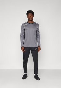 Grå langermet treningsskjorte med svarte detaljer og Nike-logo, kombinert med svarte tettsittende bukser med logo. Glatt, lett stoff.