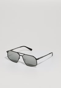 Occhiali da sole in stile black metal con lenti grigie. Forma ottagonale, aste sottili, logo su un lato e naselli trasparenti per un comfort ottimale.