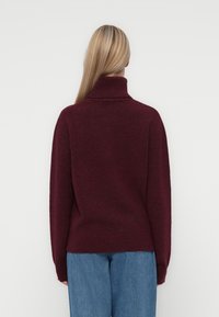 Pulover côt cu guler și manșete dublate, de culoare burgundă. Textură moale, croială lejeră și detaliu cu cusătură pe spate, asortat cu blugi de culoare albastru deschis.