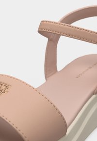 Μπεζ σανδάλι με λεπτό λουράκι στον αστράγαλο, φαρδύ λουράκι στα δάχτυλα με μεταλλικό λογότυπο και λευκή μαξιλαρωτή σόλα.