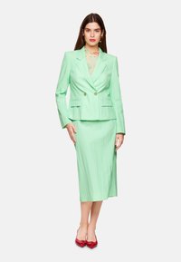 Mint green tailored suit with vertical stripes, featuring a double-breasted blazer and pencil skirt. Accented with red pointed-toe heels.