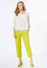 Witte, luchtige blouse met een ronde halslijn en driekwart mouwen, gecombineerd met hoge, felgroene capri-broeken en bijpassende hakken.