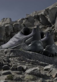 Svarta sportskor med en texturerad överdel, som har tre bandade detaljer, en förstärkt tåspets och en slitstark sula för bra grepp.