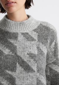 Pulover tricotat gri și alb cu un guler înalt cu nervuri, având un model geometric și o finisare moale, texturată.