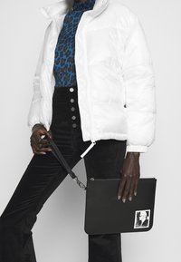 Bílá péřová bunda, modrý top s leopardím potiskem, černé manšestrové kalhoty s knoflíky. Černá psaníčko s zipem a grafickým detailem.