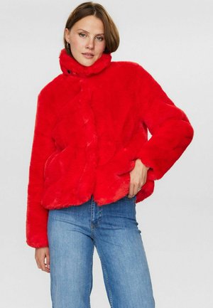 Rode nepbontjas met een hoge kraag, voorzien van een knoopsluiting, lange mouwen en een cropped pasvorm. Gedragen over blauwe jeans.