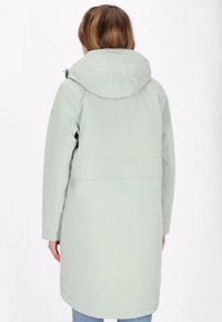 Caban impermeabil de culoare verde deschis, cu glugă, mâneci lungi și croială dreaptă. Include un brâu și are o textură netedă. Vedere din spate.