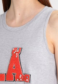 Grå ærmeløs top med et stort rødt tekstureret bogstav "A" udsmykket med blå og klare rhinsten og perler.