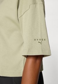 Olivgrünes kurzärmliges Hemd aus weicher Baumwolle. Verfügt über ein HYROX-Logo und ein kleines Puma-Emblem am Ärmel. Einfaches und lässiges Design.