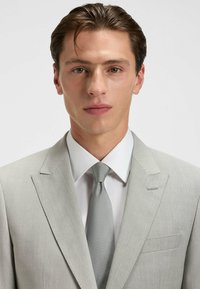 Jasnoszary garnitur o subtelnej fakturze, biała koszula i pasujący szary krawat. Posiada klapy z wycięciem i pojedynczą kieszeń na piersi.