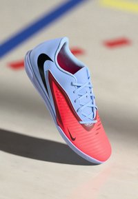 Buty sportowe Nike z jasnoniebieską górą, czerwonym gradientem po boku, czarnym logo i teksturowanymi akcentami. Sznurowany design z smukłą sylwetką.