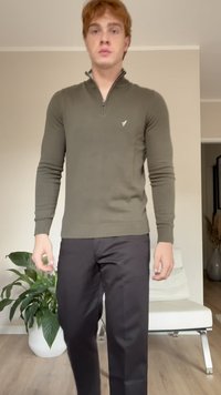 Olive green knit pullover with a zip collar, paired with black trousers. Smooth texture, fitted design, and minimalistic branding on the chest.