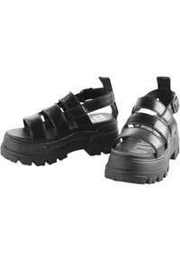Black platform sandals feature thick, textured soles, multiple wide straps, and a buckle closure, highlighting a robust and modern design.