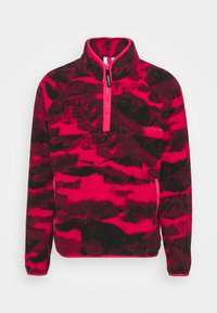 Pullover in pile di colore rosa brillante e motivo camouflage nero, con colletto alto e zip a metà, e logo adidas sul petto.