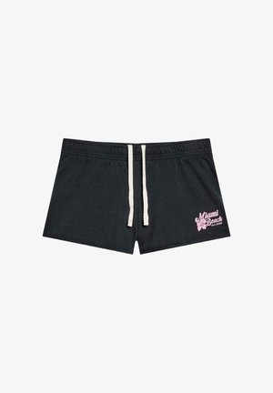 Schwarze Badeshorts mit weißem Kordelzug und rosa "Miami Beach"-Schriftzug sowie Hibiskusblume am linken Bein.
