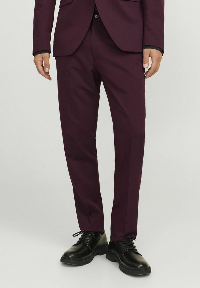 Burgundi színű, slim fit fazonú öltönynadrág, lapos elülső résszel és oldalsó zsebekkel. Sima anyagból készült, fekete fűzős cipőkkel párosítva.