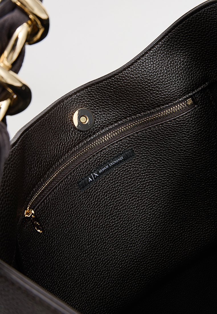 Wnętrze czarnej torebki skórzanej o fakturze, z zamykaną na zamek kieszenią oraz metką z logo. Złote akcenty sprzętowe podkreślają design.