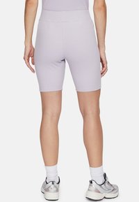 Vrouw in lichtpaarse geribbelde bike shorts, witte sokken en zilveren FILA sneakers, gezien vanaf de achterkant op een witte achtergrond.