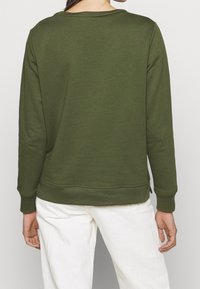 Olivgrön sweatshirt med lång ärm, ribbade ärmslut och rund halsringning. Materialet är mjukt och har en enkel design utan synliga mönster.