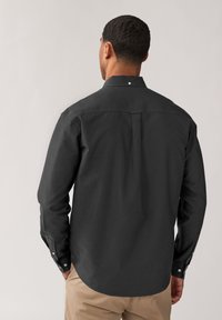 Camicia grigia scura con colletto a punta, maniche lunghe e una piega posteriore singola. Presenta polsini con bottoni e orlo arrotondato.