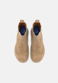 Botine din suede bej, cu panouri elastice laterale, cu bucle de prindere și tălpi interioare bleumarin. Textură netedă și design cu vârf rotunjit. Talpă plată din cauciuc.