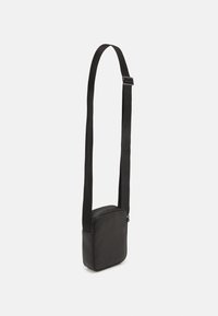 Borsa a tracolla nera con finitura testurizzata, forma squadrata, tracolla regolabile e chiusura con zip. Design minimalista adatto per un uso casual.