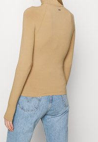 Femme portant un haut à manches longues côtelé beige et un jean en denim bleu clair taille haute, vue de dos.