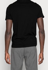 Camiseta negra de manga corta en una suave mezcla de algodón con un cuello redondo, combinada con pantalones gris oscuro de corte ajustado. Diseño minimalista, sin logotipos visibles.