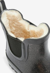 Svart gummistövlar med texturerad fuskpälsfoder, elastisk sidopanel och ett prickigt mönster på utsidan. Rund tå och kraftig sula.