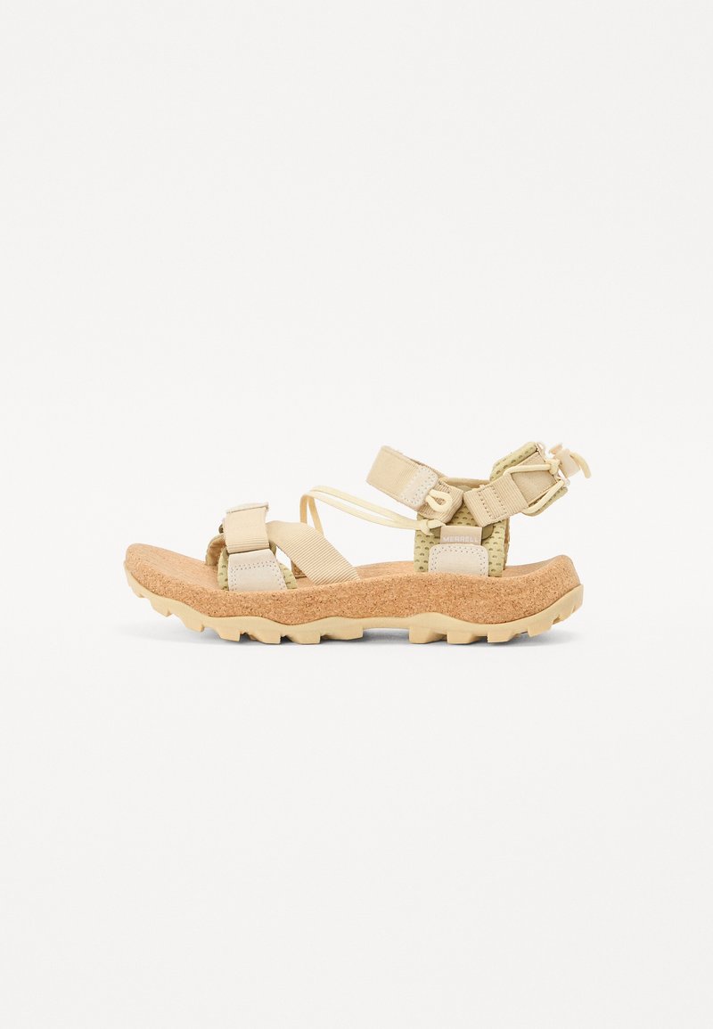 Beige outdoor sandal with cork sole, adjustable straps, textured accents, and a rugged tread pattern for enhanced grip.