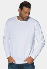 Weißes langärmeliges T-Shirt aus Baumwolle mit rundem Ausschnitt und minimalistischem 'JP'-Logo auf der Brust, kombiniert mit blauen Jeans.