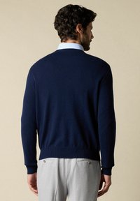 Námořnický pletený svetr s dlouhými rukávy, kulatým výstřihem a ribbovaným lemem. V kombinaci se světle šedými kalhotami, které mají dvě zadní kapsy.