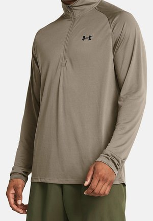 Pull léger à manches longues de couleur vert olive, avec un col montant et une fermeture éclair sur un quart. Présente un logo noir sur la poitrine et des poignets ajustés.