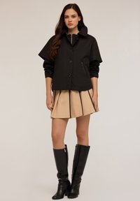 Jachetă neagră ușoară cu un design structurat, guler mare și închidere cu nasturi, asociată cu o fustă crem cu dungi negre.