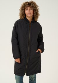 Schwarze gepolsterte Jacke mit Reißverschluss, geripptem Kragen, zwei Seitentaschen und knielangem Schnitt. Der Stoff wirkt glatt und strapazierfähig.