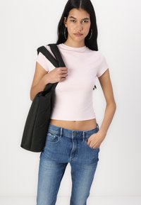 Lys rosa tettskjorte med korte ermer, parret med blå jeans. Modellen holder en mørk, polstret skulderveske med en glatt tekstur.