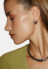 Silver spiralformade örhängen pryder örat, kombinerade med ett metalliskt halsband. Bakgrunden är enkel vit och framhäver smyckena.