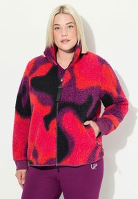 Veste en polaire dans un motif tourbillon vibrant de rose, violet et noir ; dotée d'un col haut, d'une fermeture éclair sur toute la longueur et de poches latérales.