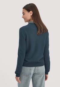 Dunkelblauer Pullover mit Rundhalsausschnitt, gerippten Bündchen und Saum, aus einem weichen Material, kombiniert mit hellblauen Jeans.