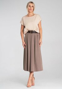 Beżowa bluzka z krótkim rękawem o teksturowanej tkaninie; brązowa spódnica plisowana z szerokim pasem i srebrnym zapięciem; jasne buty.