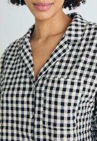 Svart och gräddfärgad gingham-rutigt skjorta med krage, framficka och knappstängning, tillverkad av ett lättviktig material.
