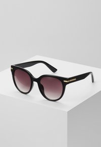 Black sunglasses with a glossy finish, oversized round lenses transitioning from dark to lighter shades, and gold-tone accents on the arms.