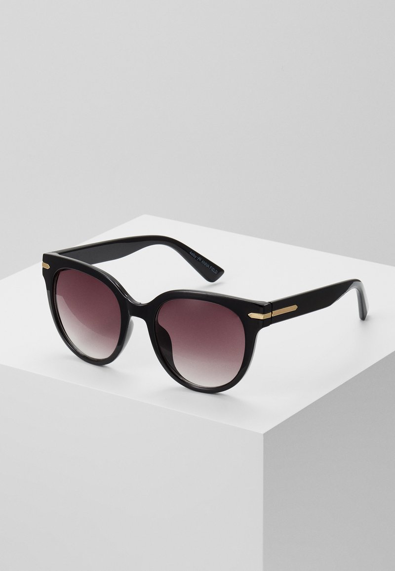 Black sunglasses with a glossy finish, oversized round lenses transitioning from dark to lighter shades, and gold-tone accents on the arms.