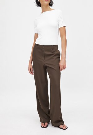 Hvid tætsiddende kortærmet top med rund halsudskæring, parret med højtaljede brune brede bukser. Sorte flip-flops med strukturerede stropper.