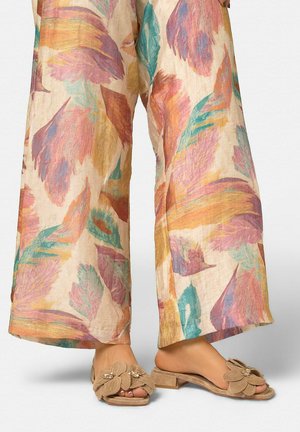 Vedere a picioarelor cu pantaloni largi, lejeri, cu imprimeu pastelat cu pene, asortați cu sandale bej, cu toc mic, cu vârf deschis, decorate cu aplicații florale.