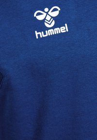 T-shirt in cotone blu con logo bianco 'hummel' decorato con un design di ape e una leggera texture. Maniche corte e scollatura rotonda.