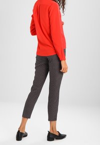 Blusa rossa a maniche lunghe abbinata a pantaloni tapered a righe bianchi e neri, completata da scarpe slip-on nere. Tessuto morbido e vestibilità su misura.
